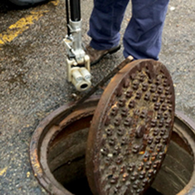 an employee opens a man hole cover to checks a portion of the sewer