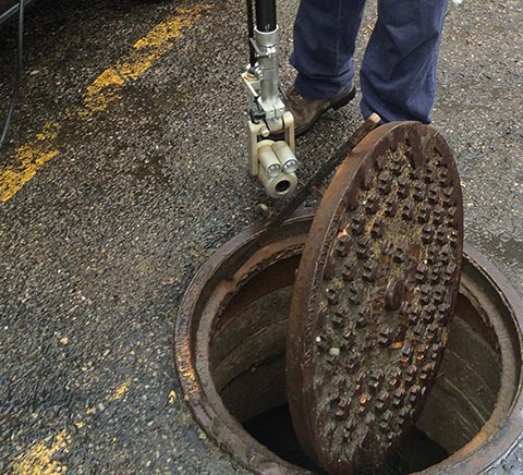 Person using a tool to open a utility hole cover